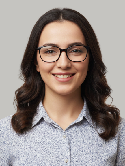 Smiling woman with dark hair and glasses wearing a light patterned button-down shirt against a gray background (head-and-shoulders portrait).